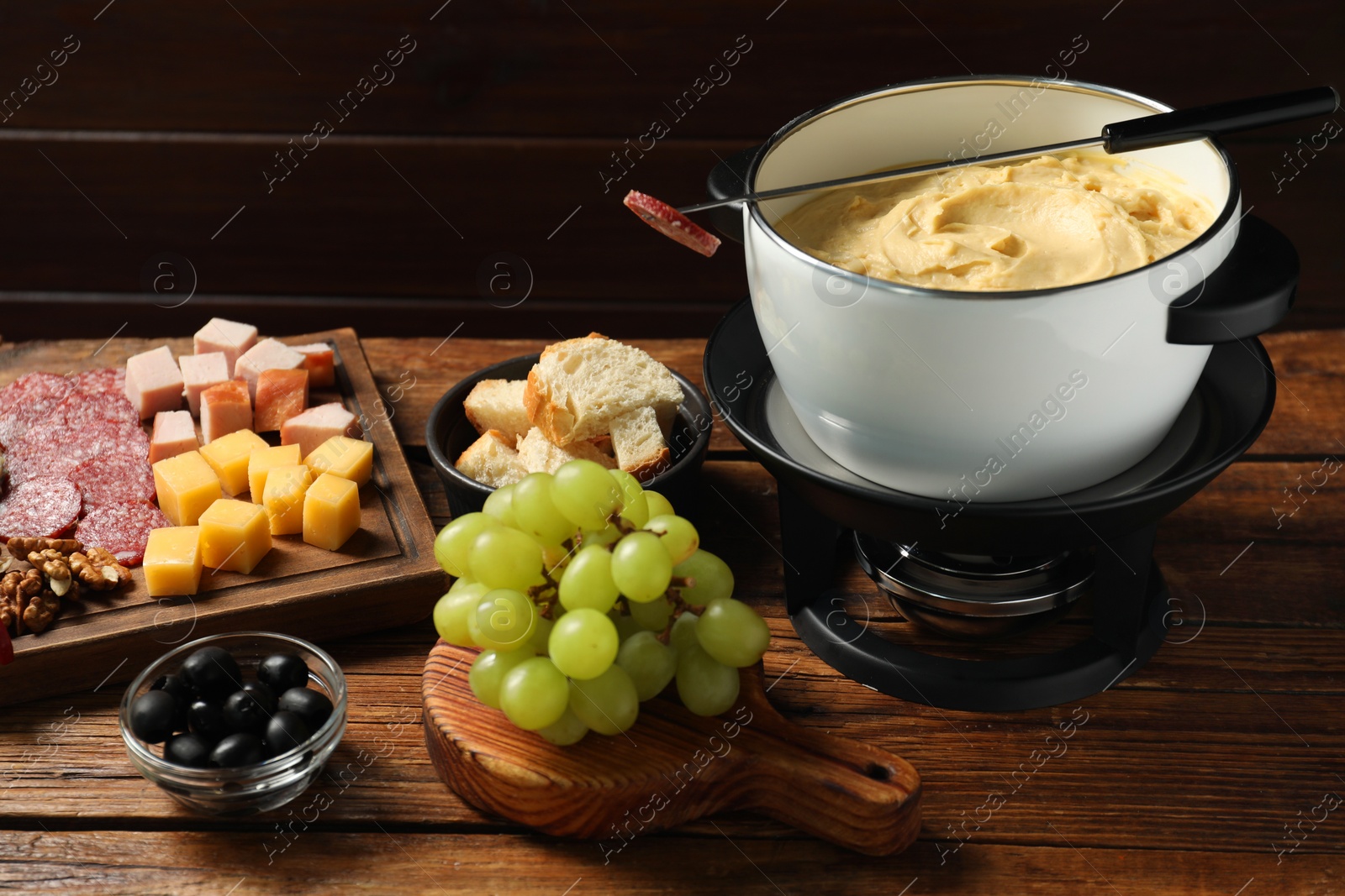 Photo of Fork with piece of sausage, melted cheese in fondue pot and other products on wooden table