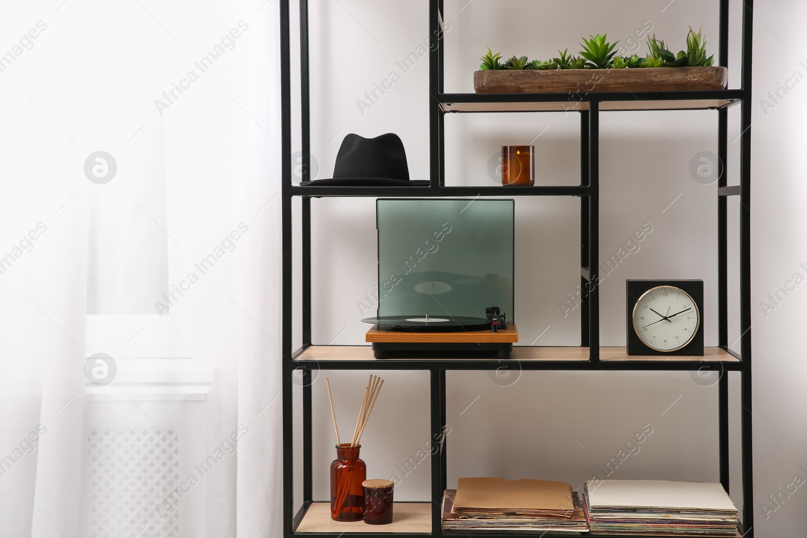 Photo of Stylish turntable with vinyl record on shelving unit indoors