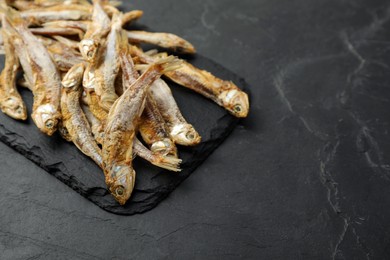 Photo of Delicious dried anchovies on black table, closeup. Space for text