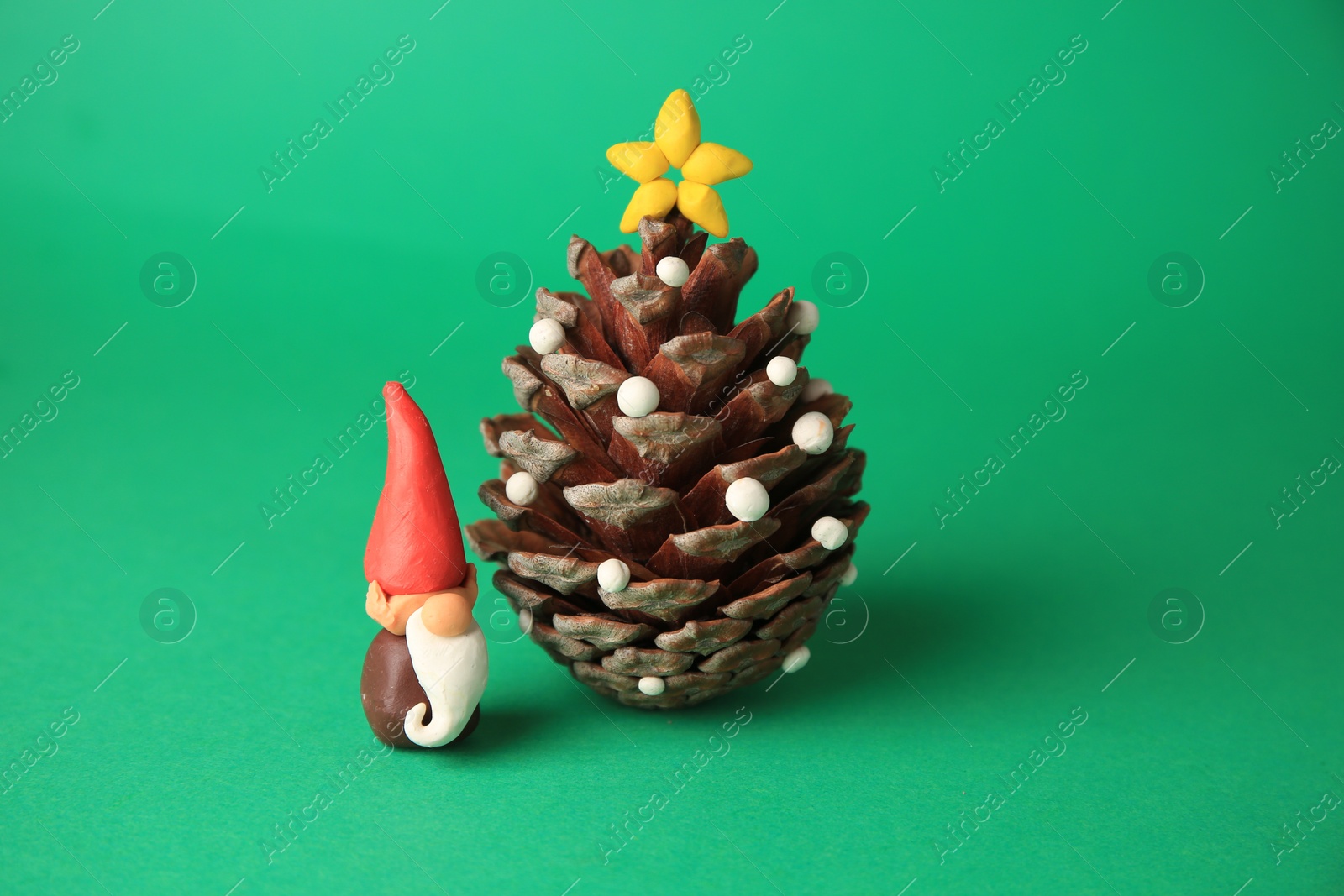 Photo of Beautiful plasticine dwarf with pinecone on green background. Children's handmade ideas