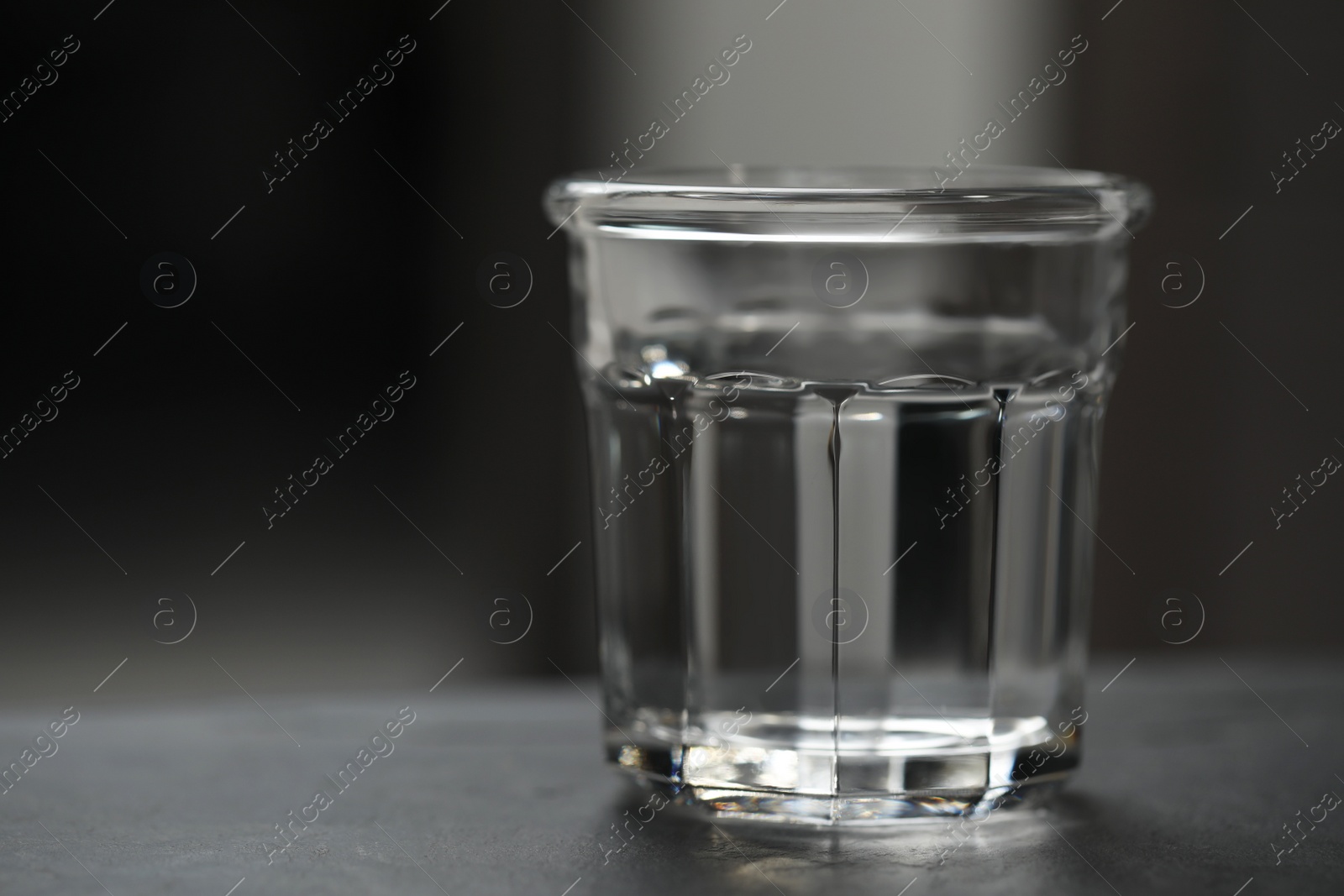 Photo of Glass of pure water on black table against blurred background, space for text