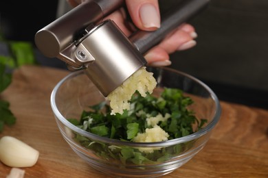 Photo of Woman squeezing garlic with press at wooden table, closeup