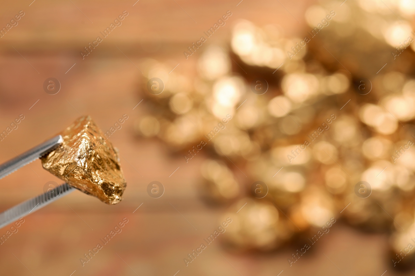 Photo of Tweezers with gold nugget against blurred background, closeup. Space for text