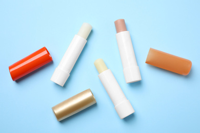Photo of Hygienic lipsticks on light blue background, flat lay