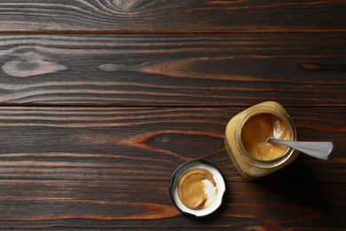 Photo of Spicy mustard and spoon in glass jar on wooden table, top view