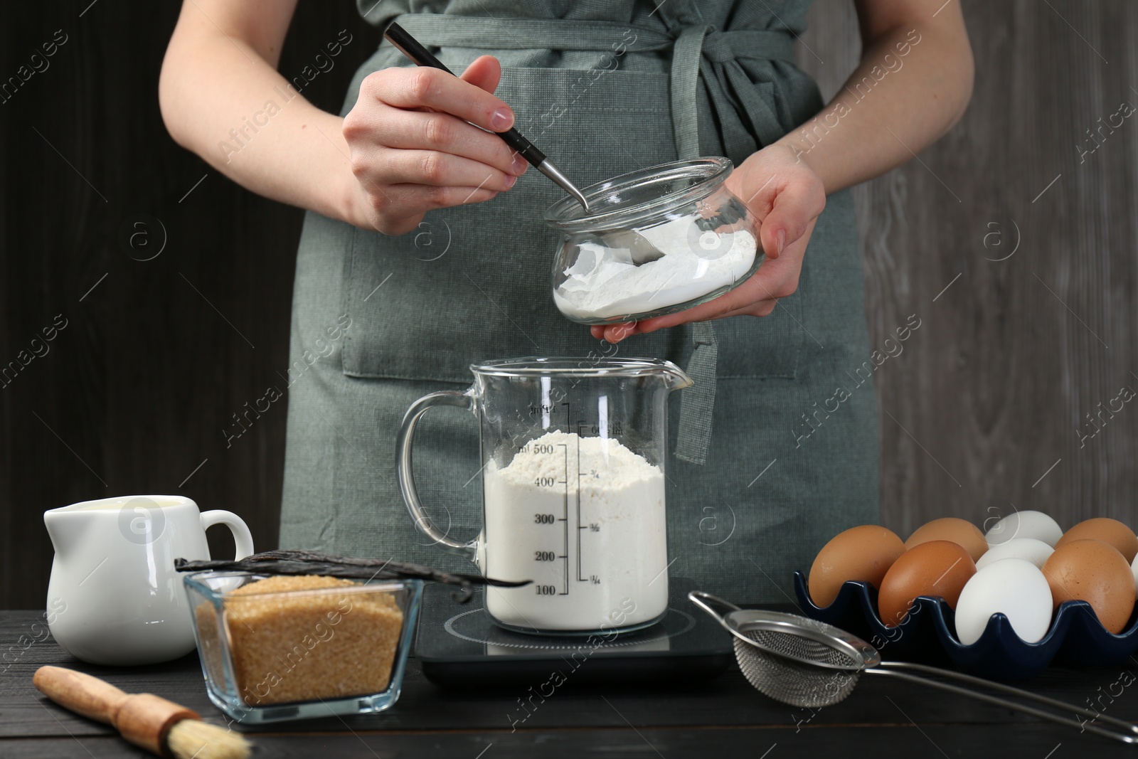 Photo of Woman adding baking powder into measuring cup at black wooden table, closeup