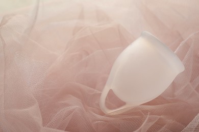 Photo of Menstrual cup on pink fabric, closeup. Space for text
