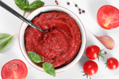 Photo of Tasty tomato paste in bowl and ingredients on white table, flat lay