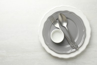 Stylish setting with cutlery, bowl and plates on light textured table, top view. Space for text