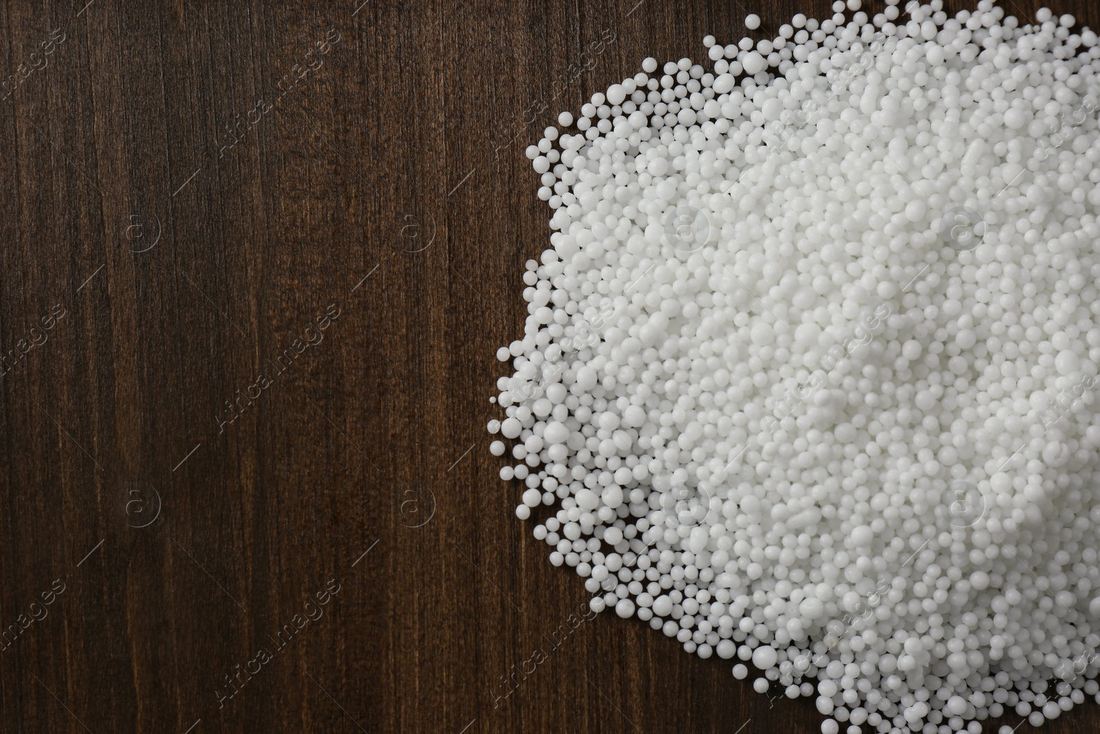 Photo of Pellets of ammonium nitrate on wooden table, flat lay with space for text. Mineral fertilizer