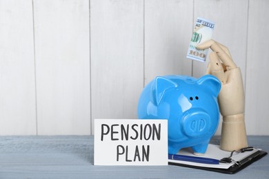 Photo of Card with phrase Pension Plan, mannequin hand holding dollar banknote and piggy bank on light blue wooden table, space for text. Retirement concept