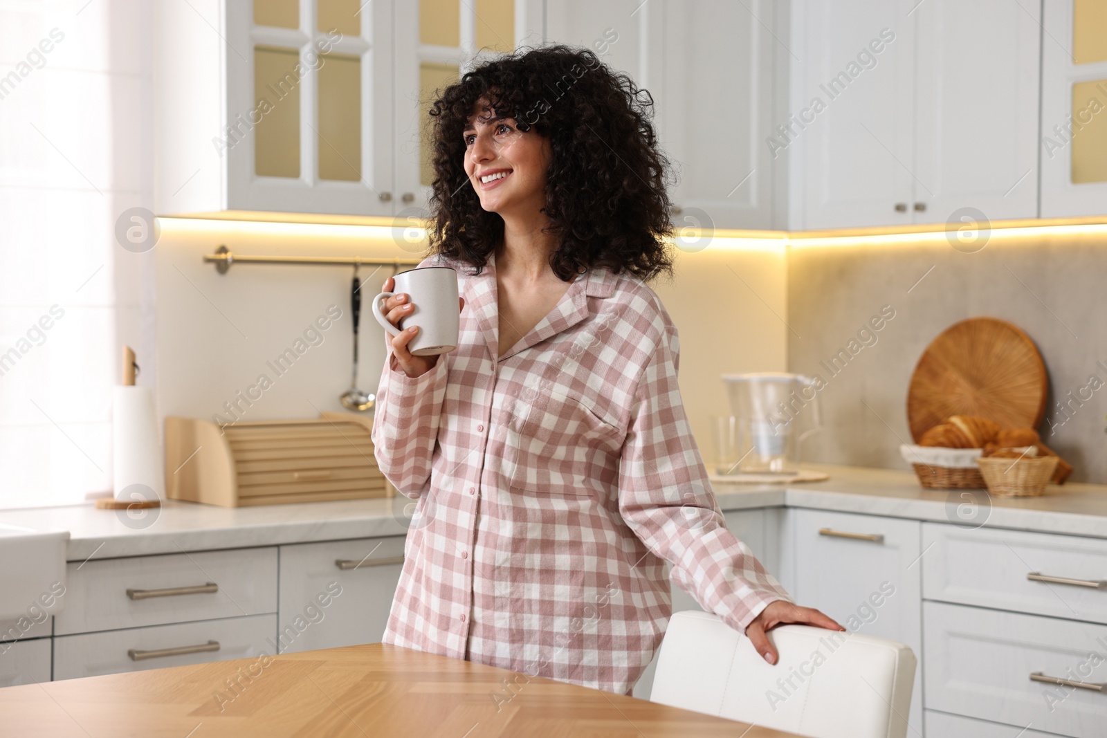 Photo of Beautiful young woman in stylish pyjama with cup of drink in kitchen