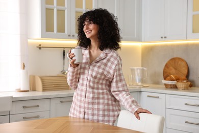 Beautiful young woman in stylish pyjama with cup of drink in kitchen