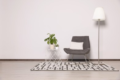 Photo of Stylish armchair, floor lamp and plants near white wall. Space for text