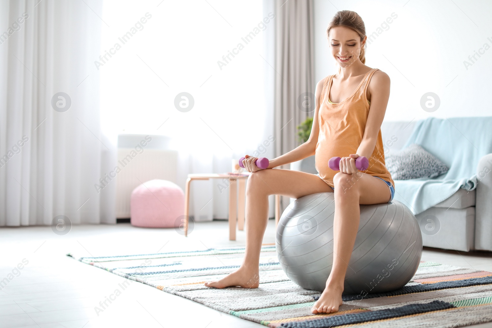 Photo of Young pregnant woman doing exercises with dumbbells at home