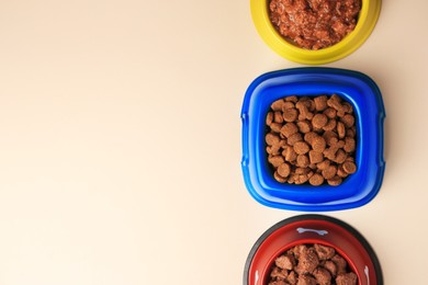 Photo of Dry and wet pet food in feeding bowls on beige background, flat lay. Space for text