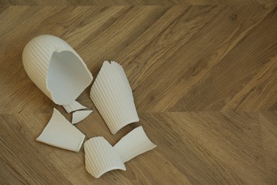 Broken white ceramic vase on wooden floor, flat lay. Space for text