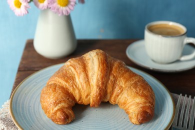 Delicious fresh croissant served with coffee on wooden table, closeup