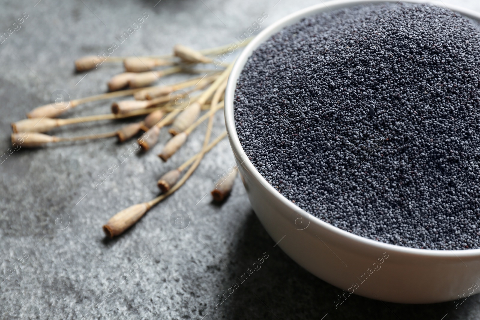 Photo of Poppy seeds in bowl on grey table, closeup. Space for text