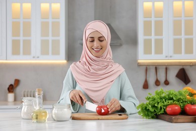 Muslim woman making delicious salad with vegetables at white table in kitchen