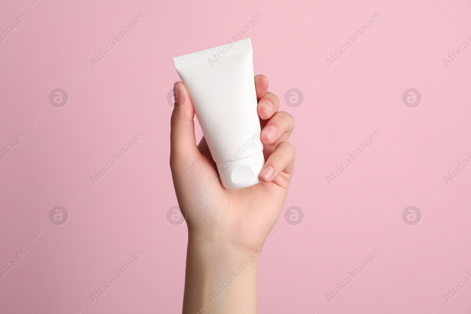 Photo of Woman holding tube of face cream on pink background, closeup