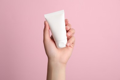 Photo of Woman holding tube of face cream on pink background, closeup