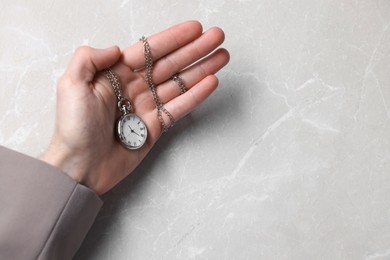Man holding chain with elegant pocket watch at light marble table, closeup. Space for text