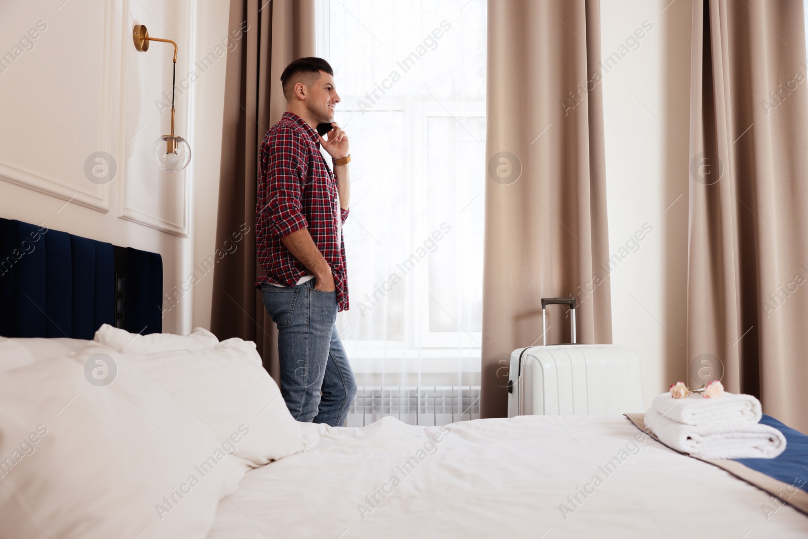 Photo of Handsome man talking on phone near window in hotel room