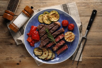 Delicious grilled beef steak with vegetables and spices on wooden table, flat lay