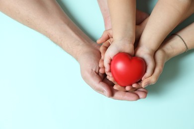 Photo of Parents and child holding red decorative heart on light blue background, top view. Space for text