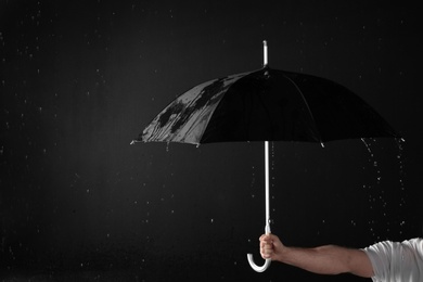 Photo of Man holding black umbrella under rain against dark background, closeup