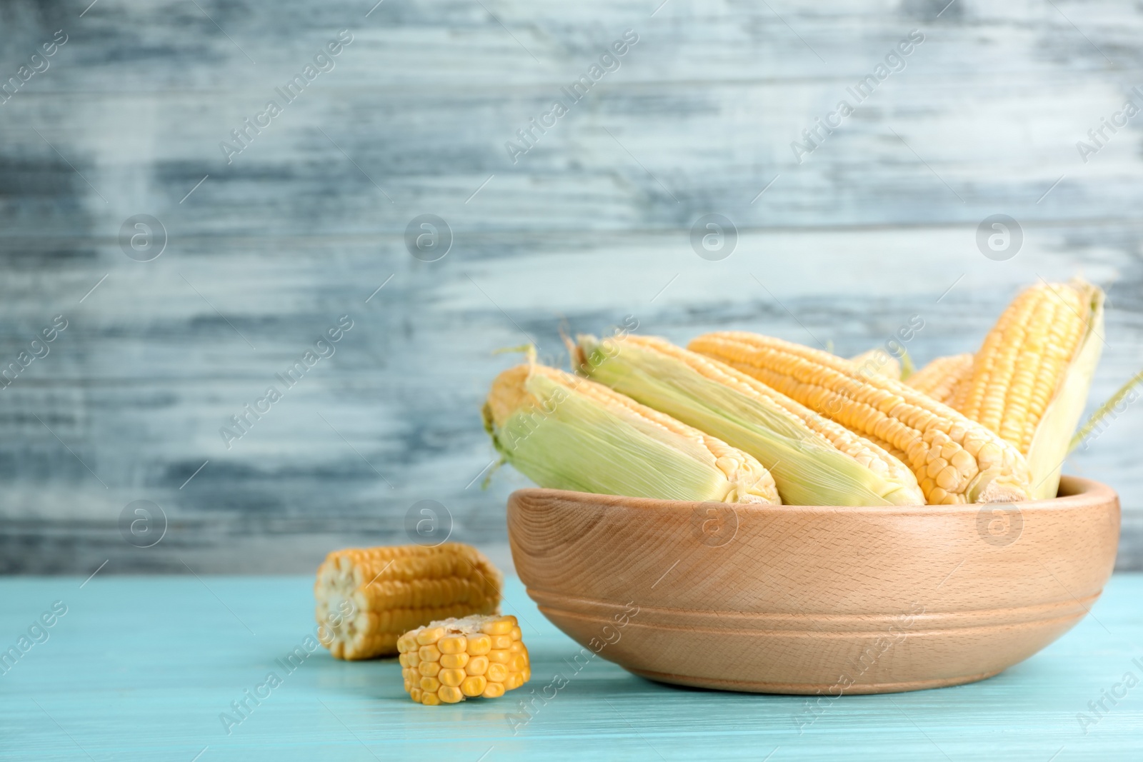 Photo of Bowl with tasty sweet corn cobs on wooden table