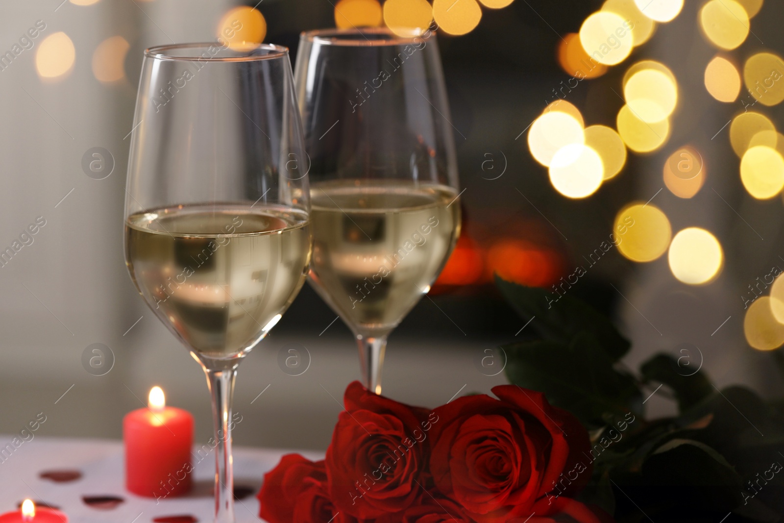Photo of Glasses of white wine, rose flowers and burning candles against blurred lights, space for text. Romantic atmosphere