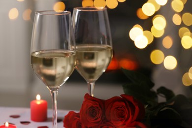 Glasses of white wine, rose flowers and burning candles against blurred lights, space for text. Romantic atmosphere