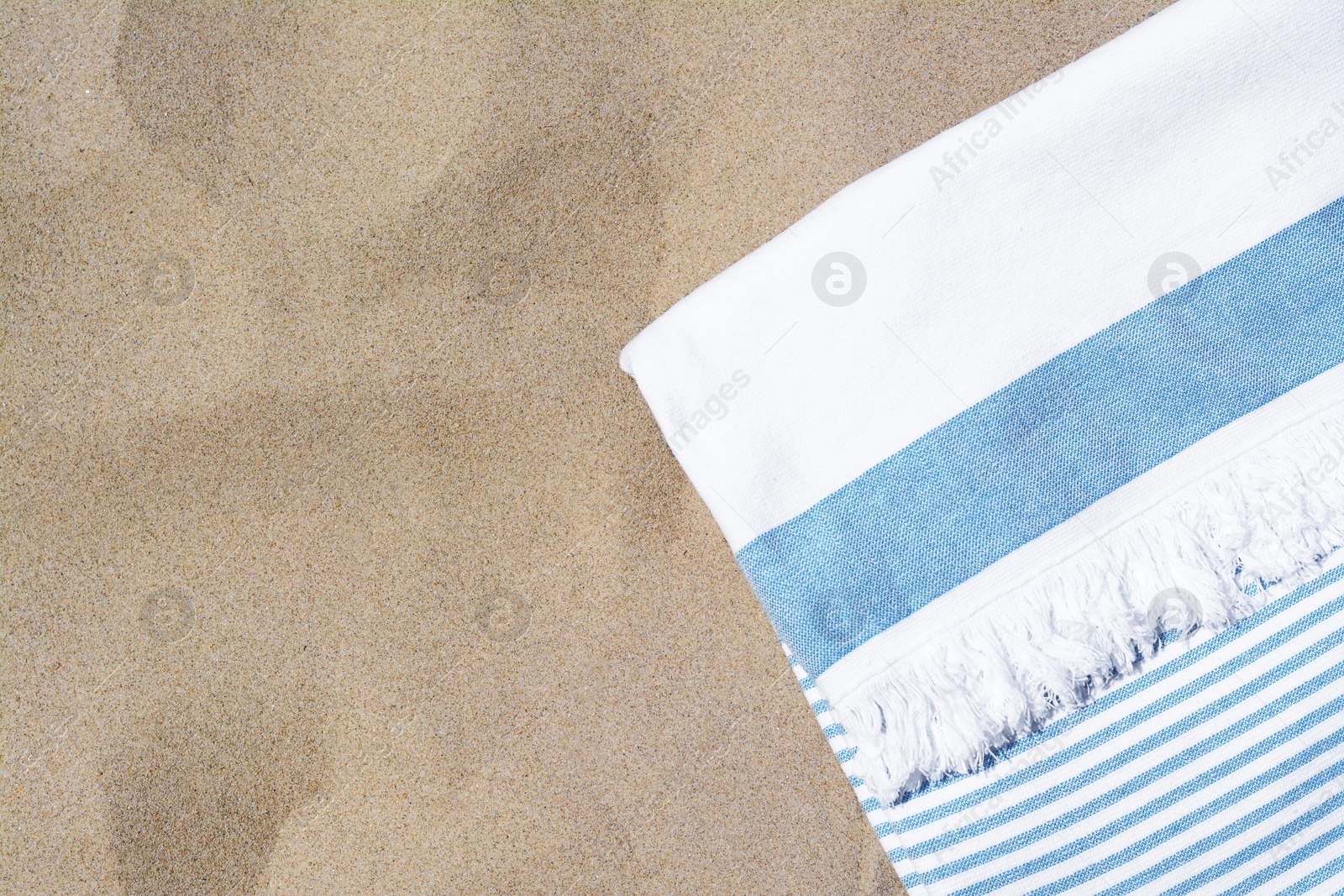 Photo of White and light blue striped towel on sandy beach, top view. Space for text