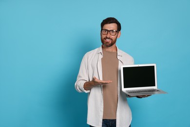 Photo of Handsome man with laptop on light blue background. Space for text