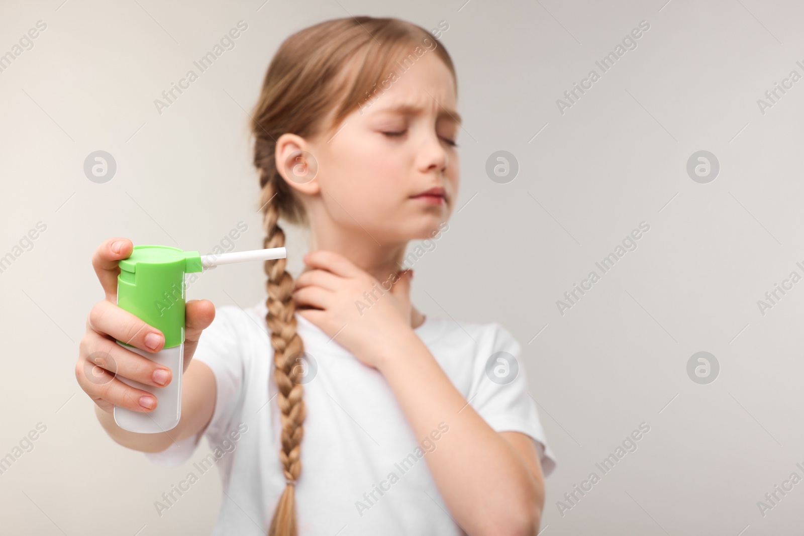 Photo of Little girl holding throat spray on light grey background, selective focus