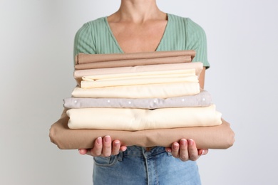 Photo of Woman holding stack of clean bed linens on light grey background