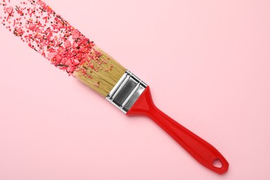 Photo of Brush painting with red sprinkles on pink background, top view. Creative concept