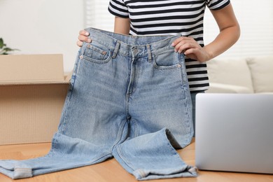 Photo of Young woman with just unpacked new jeans and laptop on wooden table indoors, closeup. Online shopping