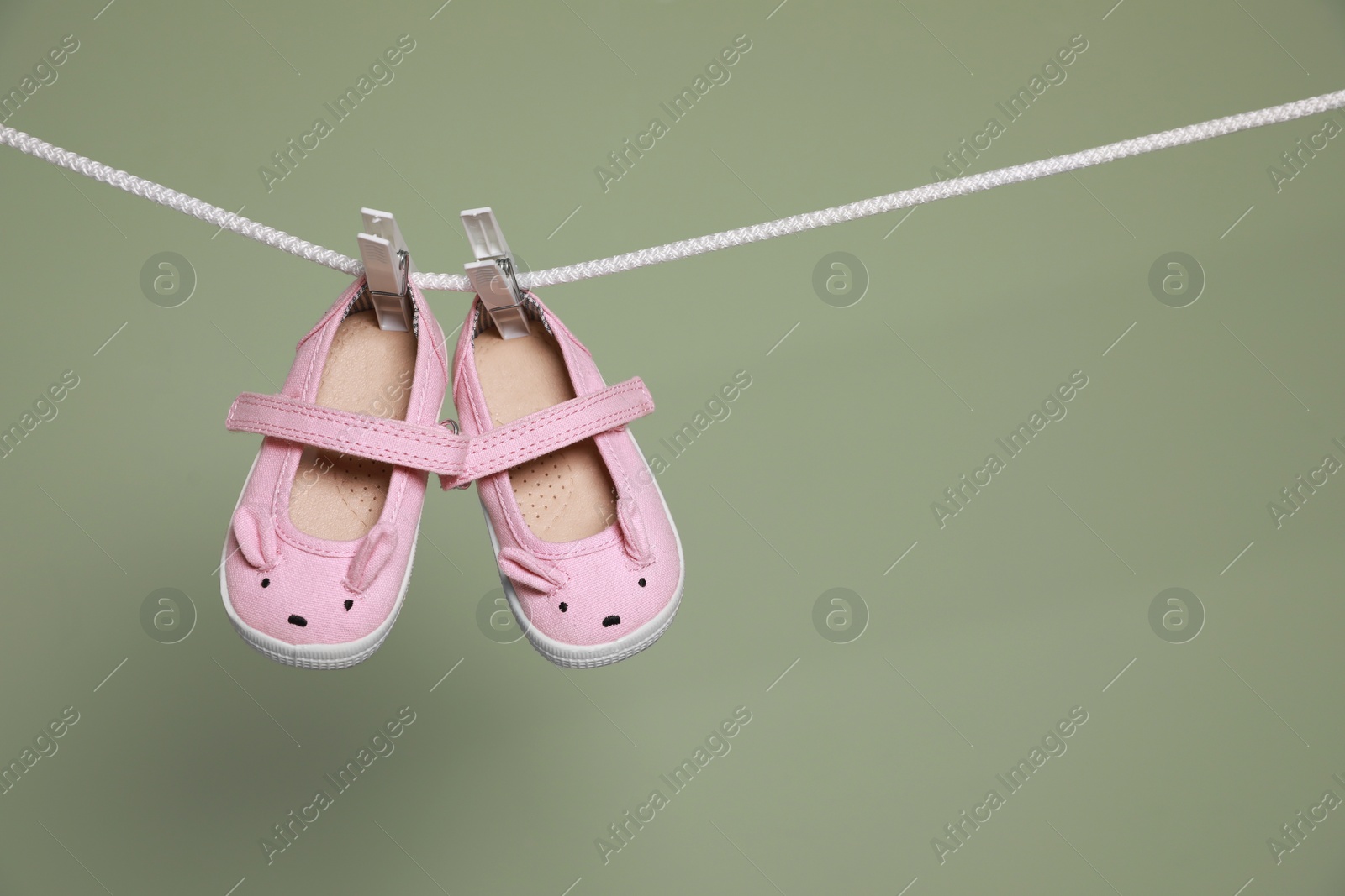 Photo of Cute small baby shoes hanging on washing line against green background, space for text