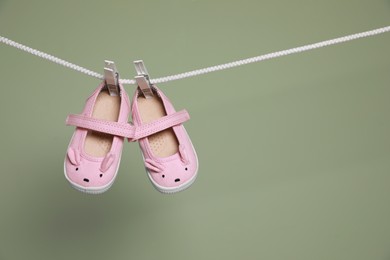 Cute small baby shoes hanging on washing line against green background, space for text