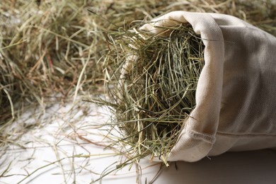 Burlap sack with dried hay on white wooden table, closeup