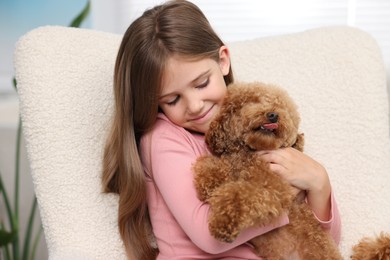 Little child with cute puppy in armchair indoors. Lovely pet