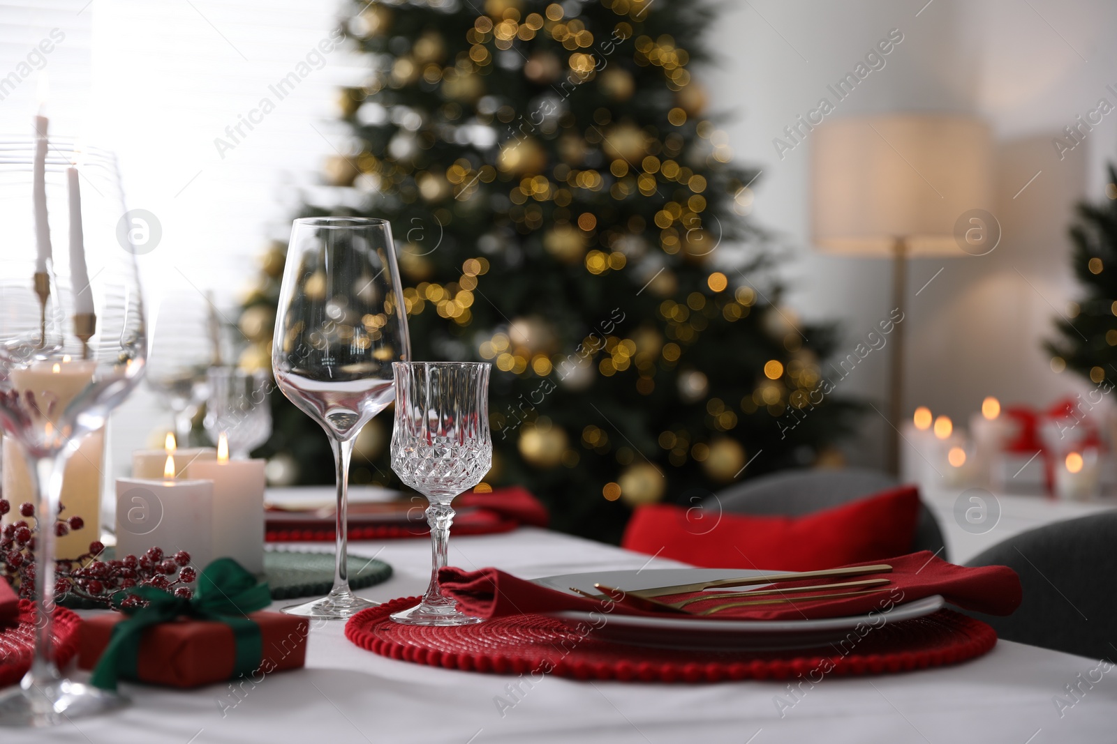 Photo of Christmas table setting with burning candles, gift box and dishware indoors