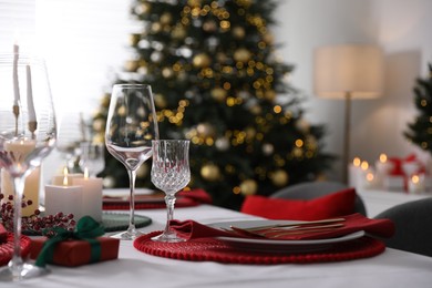 Christmas table setting with burning candles, gift box and dishware indoors