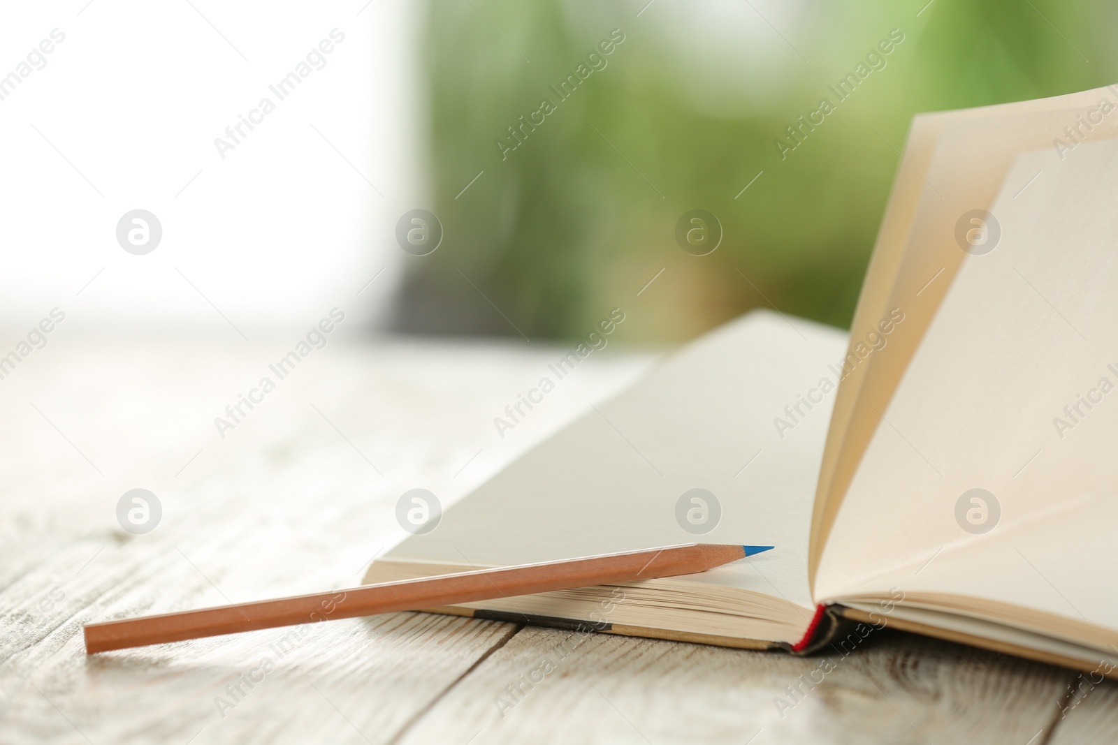 Photo of Closeup view of open notebook with pencil on white wooden table against blurred background