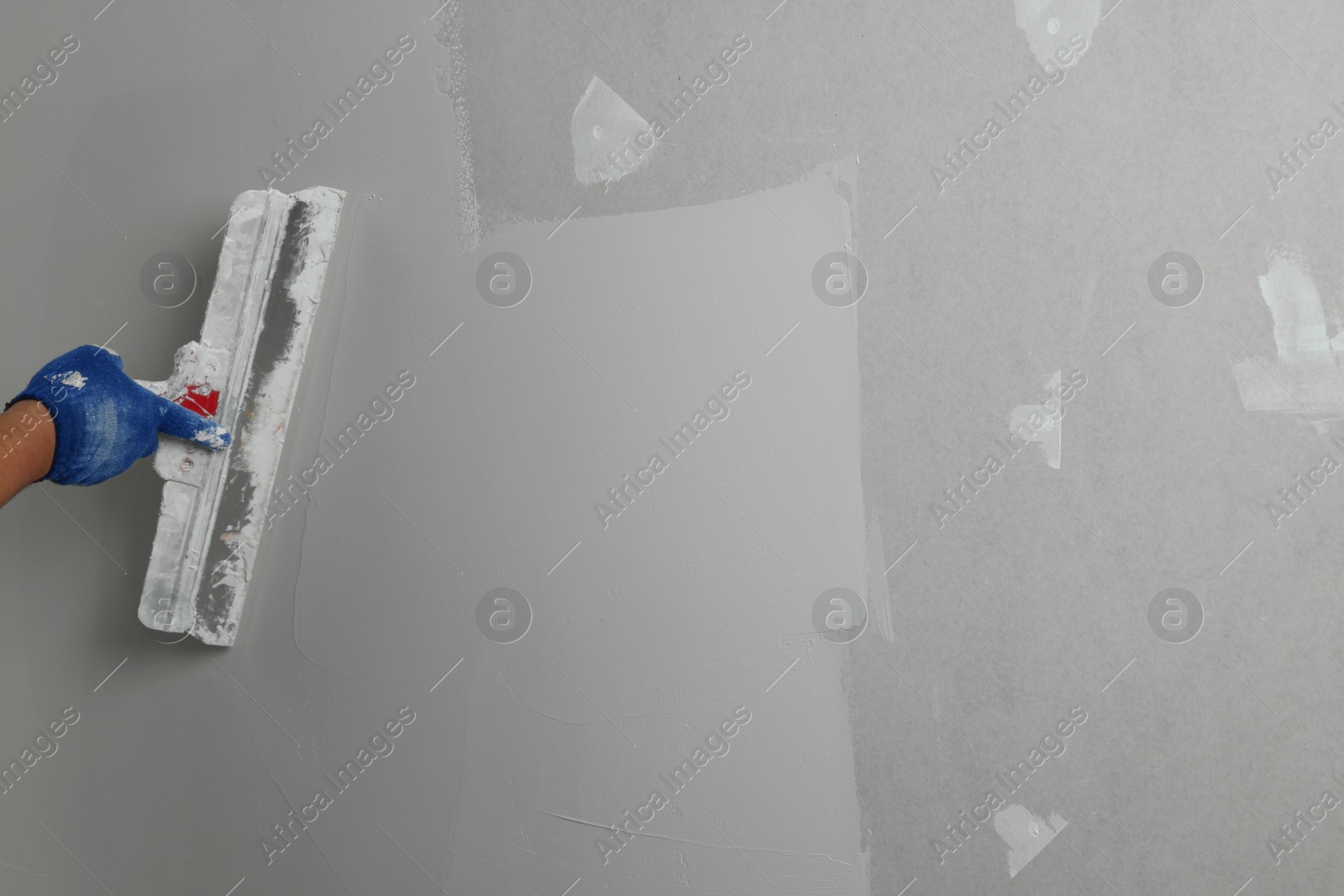 Photo of Professional worker plastering wall with putty knife, closeup