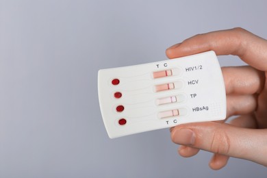 Woman holding disposable multi-infection express test on light grey background, closeup