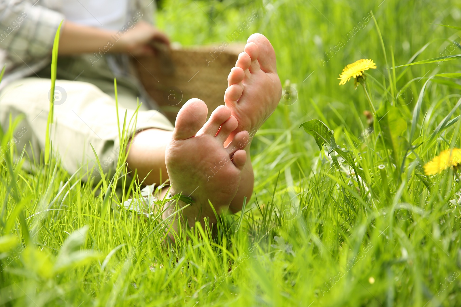 Photo of Woman sitting barefoot on green grass outdoors, closeup